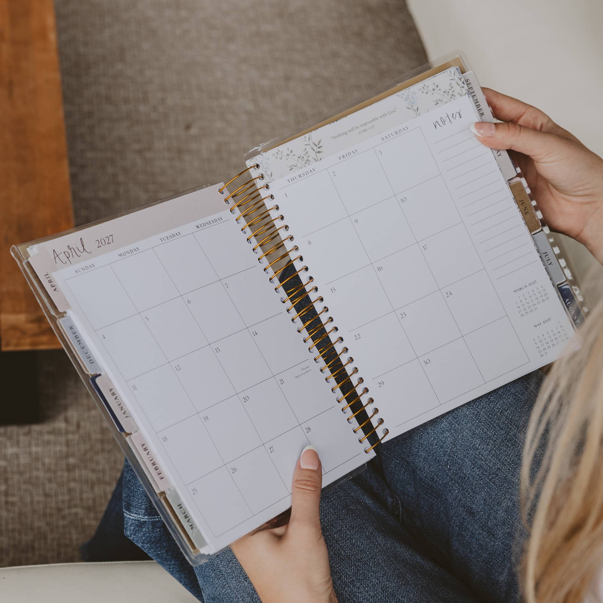 Person holding a spiral-bound planner open to a calendar page.