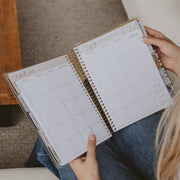 Person holding a spiral-bound planner open to a calendar page.