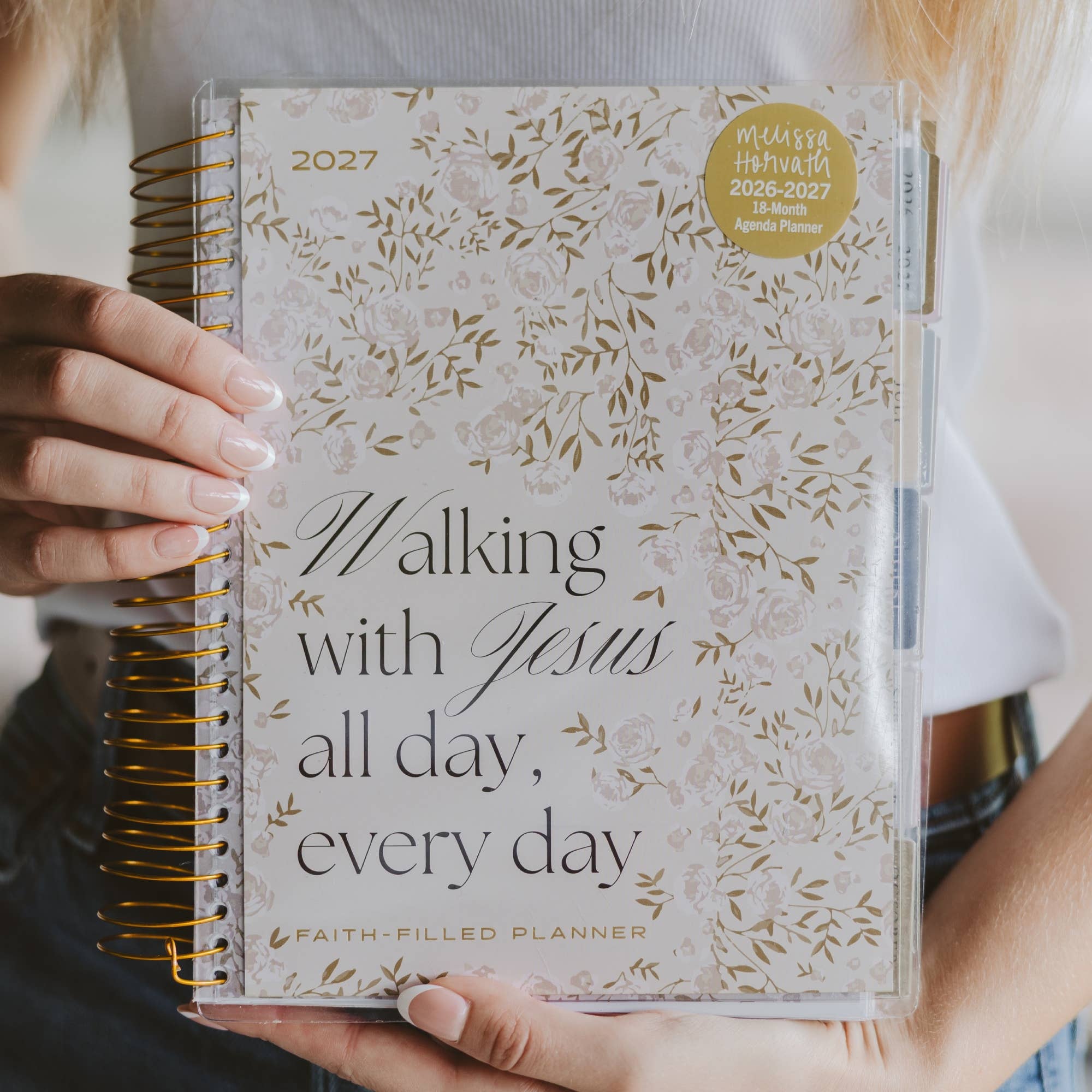 Planner with floral design and text 'Walking with Jesus all day, every day' held by a person.