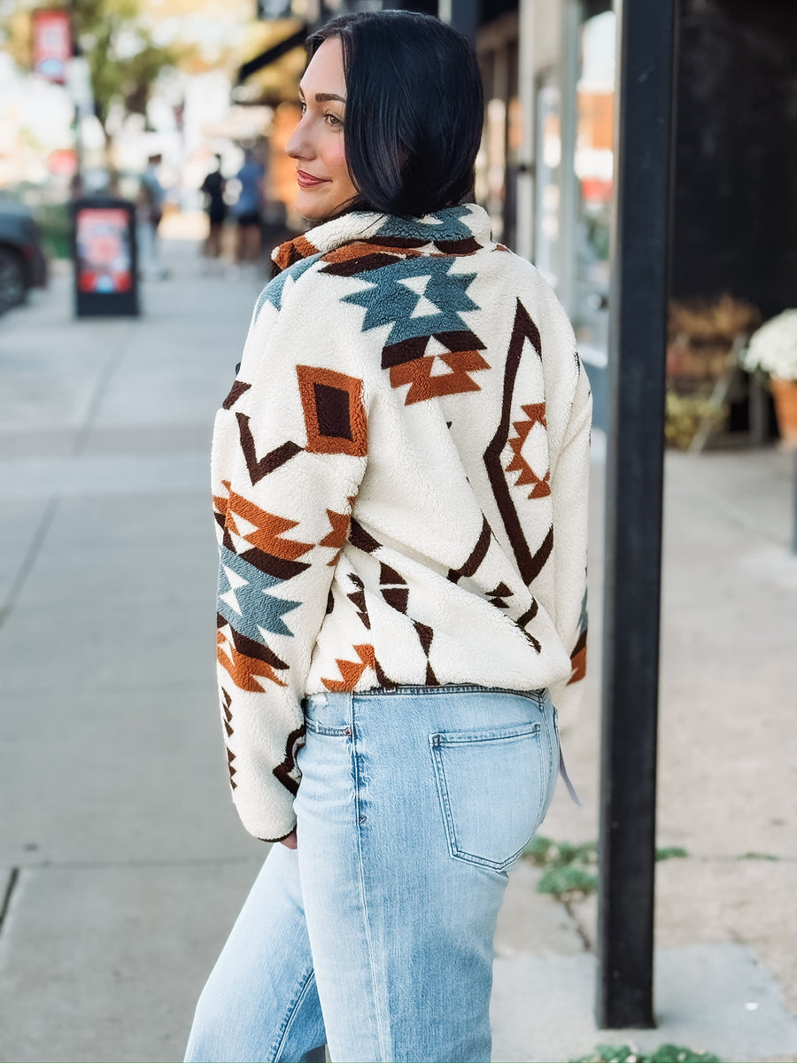 Aztec brown, rust, and turquoise print on a cream sherpa zip up jacket.