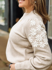 Woman wearing a beige sweater with white floral embroidered  sleeves.