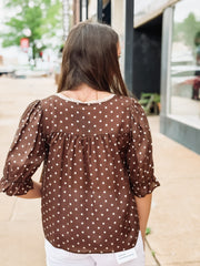 Woman wearing a brown polka dot blouse outdoors