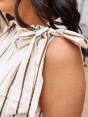 Close-up of a person wearing a white dress with brown stripes and a bow detail on the shoulder.