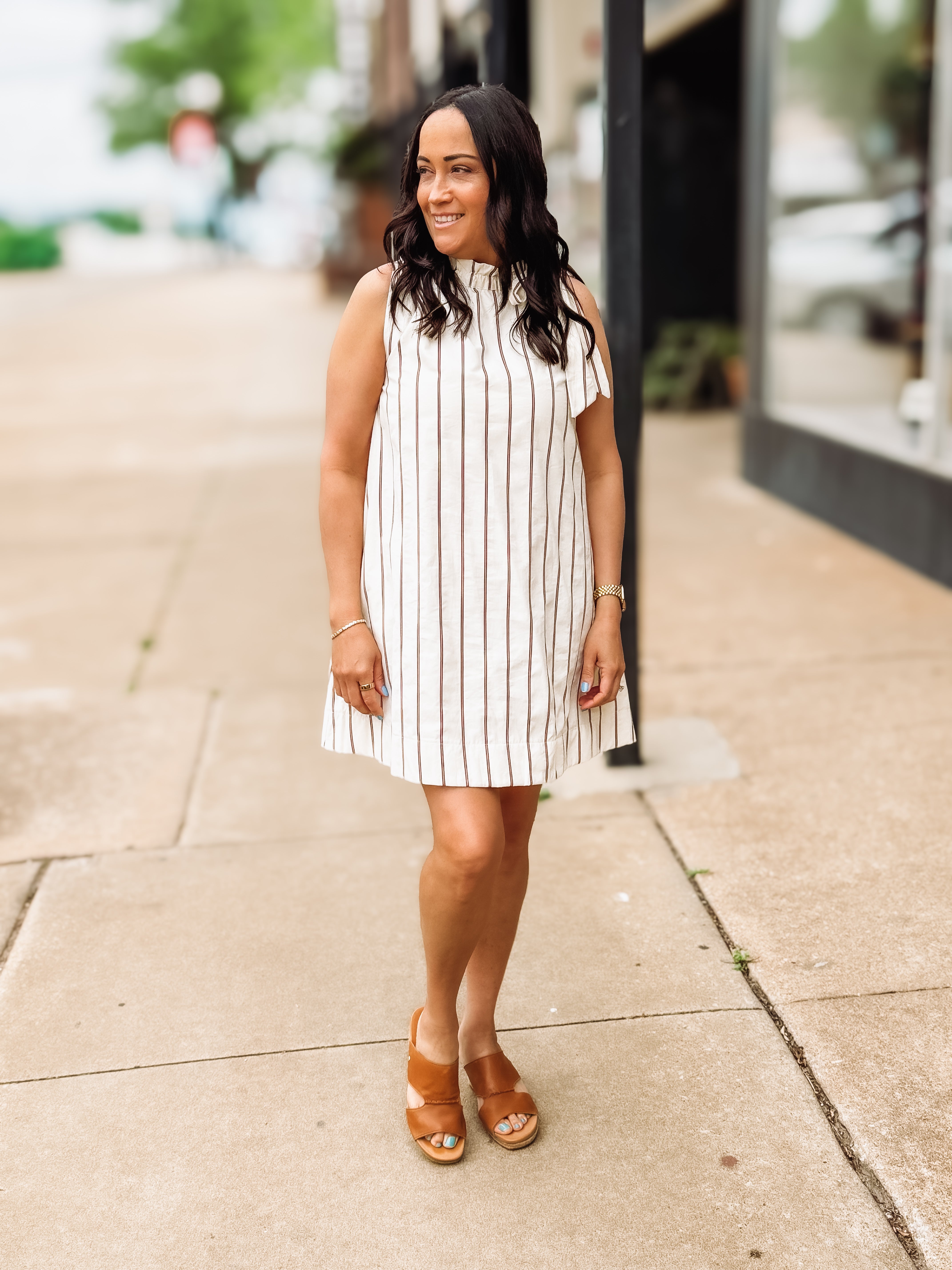 Woman in a striped dress standing on a sidewalk with a blurred street background