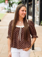 Woman wearing a brown polka dot blouse with white pants outdoors.