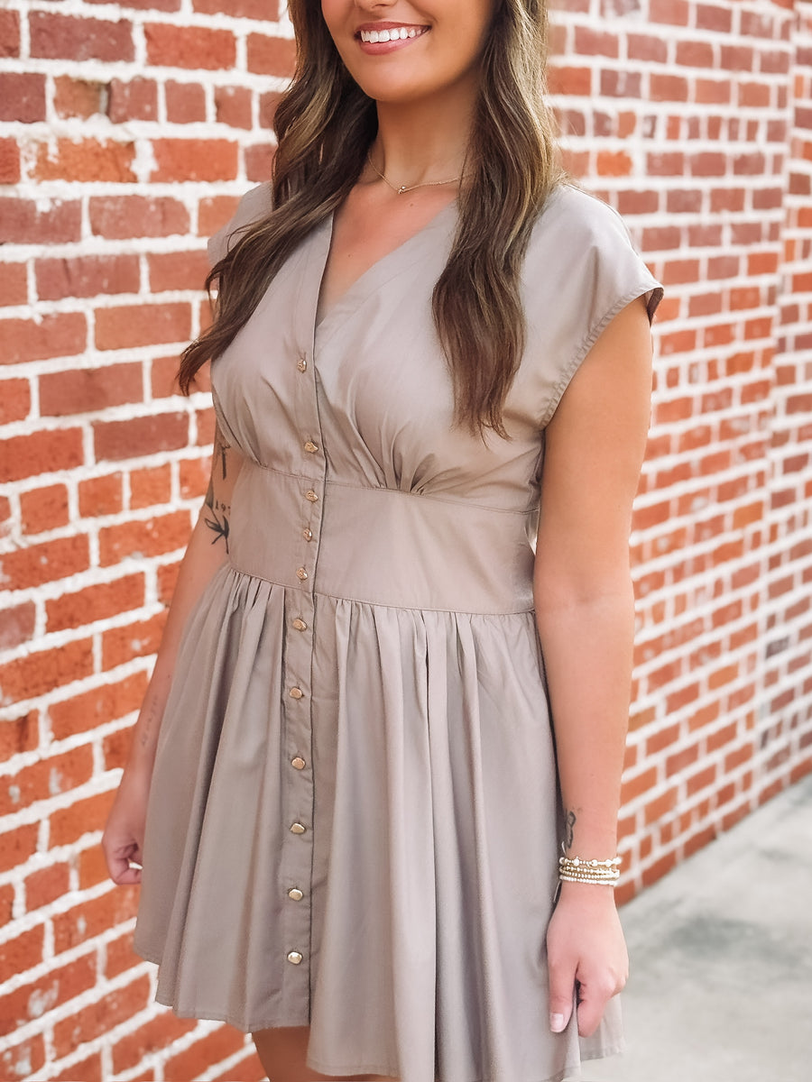 Taupe brown colored short sleeve mini dress. Features a full button front, a cinched waist and a V neckline. 