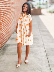 Cream mini dress with an orange polka dot print, button front closure, short sleeves, side pockets, and a relaxed fit.
