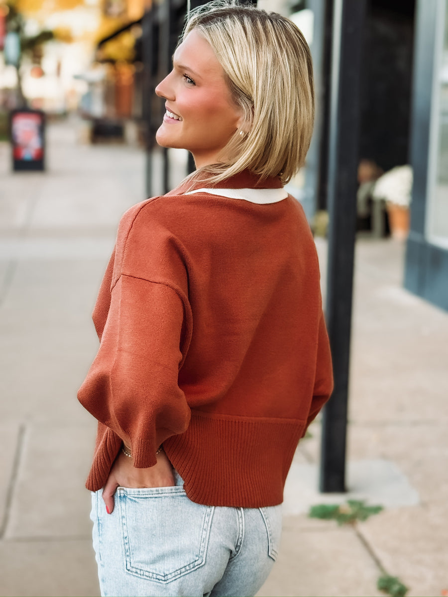 Rust drop sleeve cropped sweater with white contrast detail throughout the v neckline and front seam.