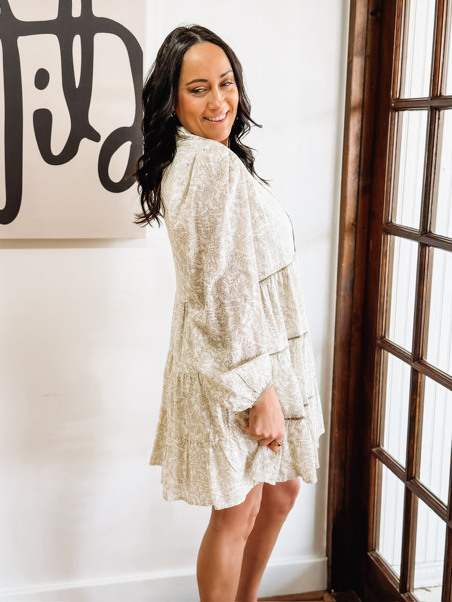 Dainty olive floral print on a cream long sleeve mini dress that features tiers and a slight v neck.