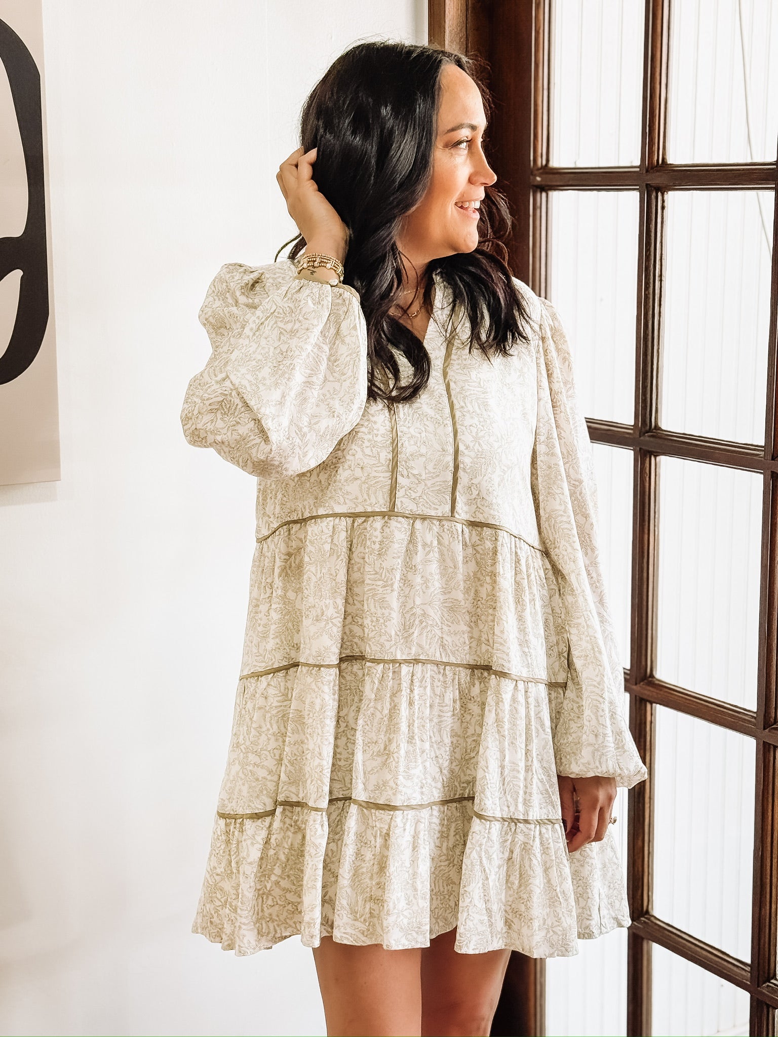 Dainty olive floral print on a cream long sleeve mini dress that features tiers and a slight v neck.