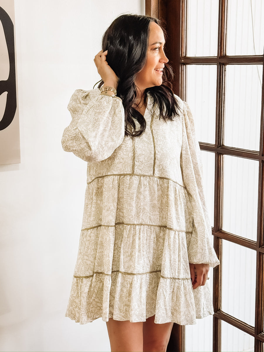 Dainty olive floral print on a cream long sleeve mini dress that features tiers and a slight v neck.