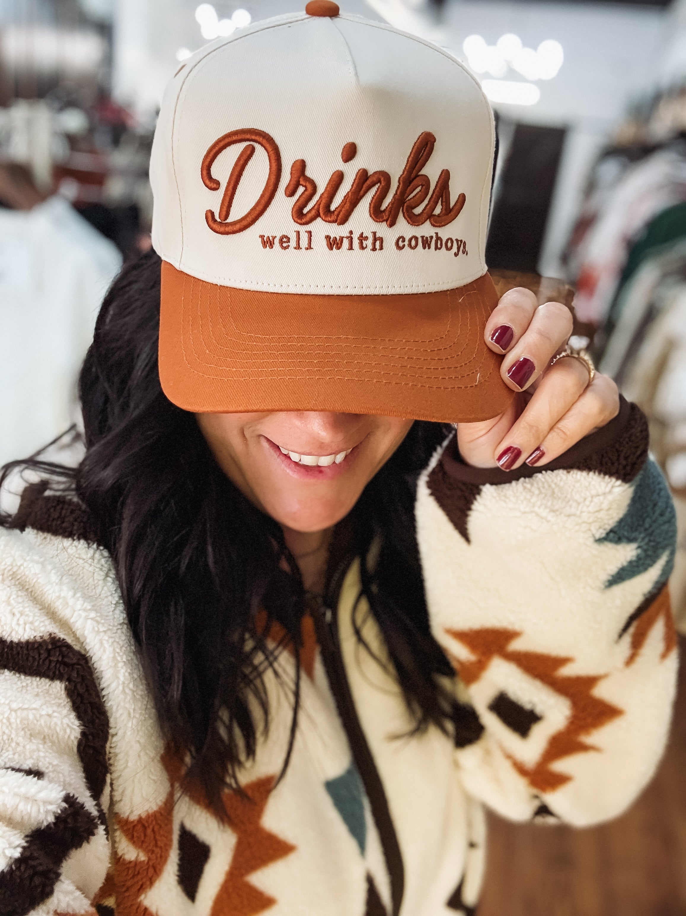 Drinks well with cowboys typography on a rust and cream canvas trucker hat.