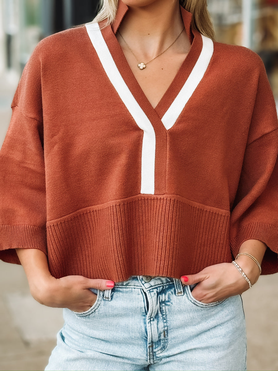 Rust drop sleeve cropped sweater with white contrast detail throughout the v neckline and front seam.