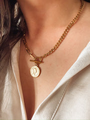 Gold mixed chain necklace with a toggle closure and a small coin pendant.