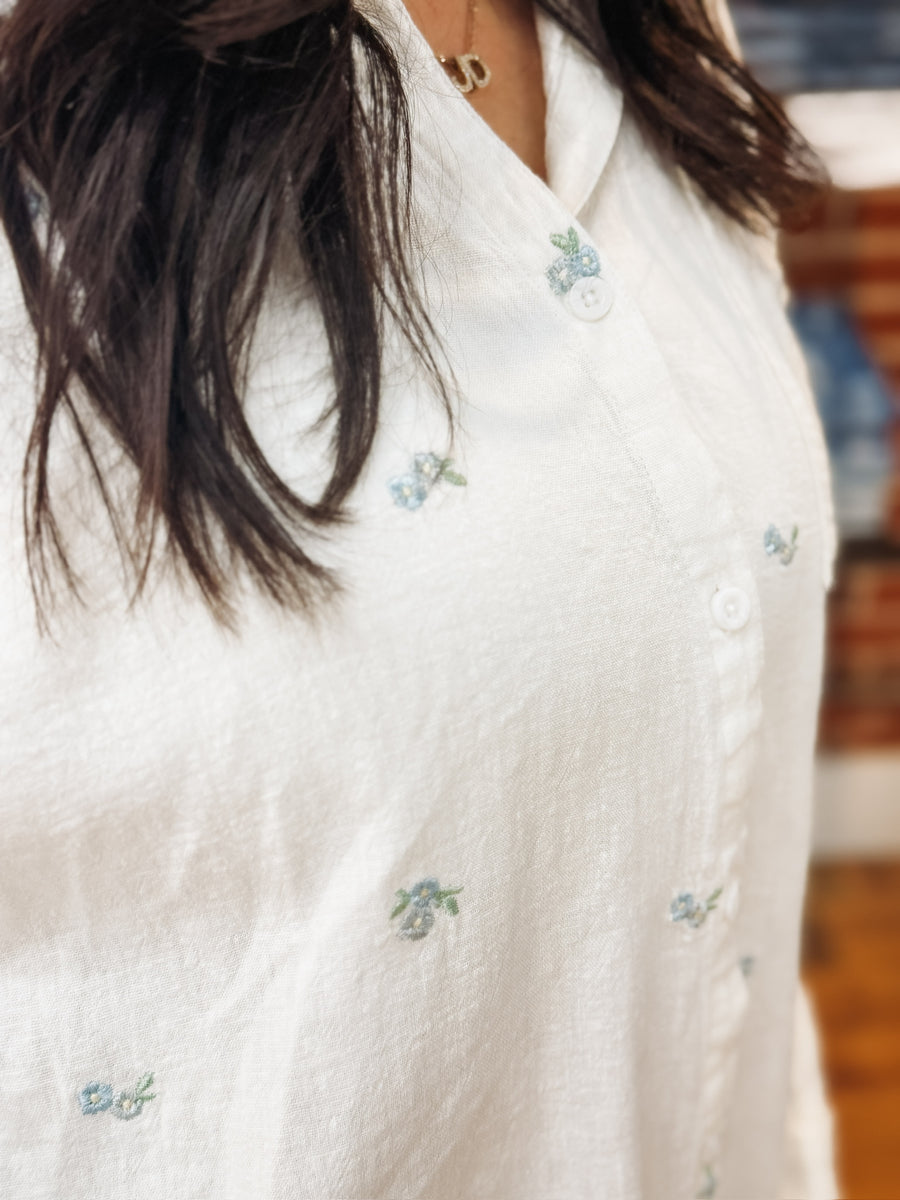 Women's white relaxed fit button up blouse with dainty blue floral embroidered detailing.