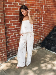 Strapless ecru matching pant  set featuring a flowy tube top with an elastic neckline and wide leg pants with an elastic drawstring waistband, pockets, and a soft light brown polka dot print.