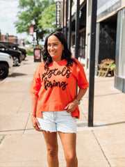 “Pistols Firing” printed in black script on an orange boxy top across the front, styled in an OSU game day theme.