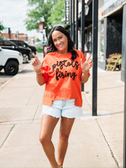 “Pistols Firing” printed in black script on an orange boxy top across the front, styled in an OSU game day theme.