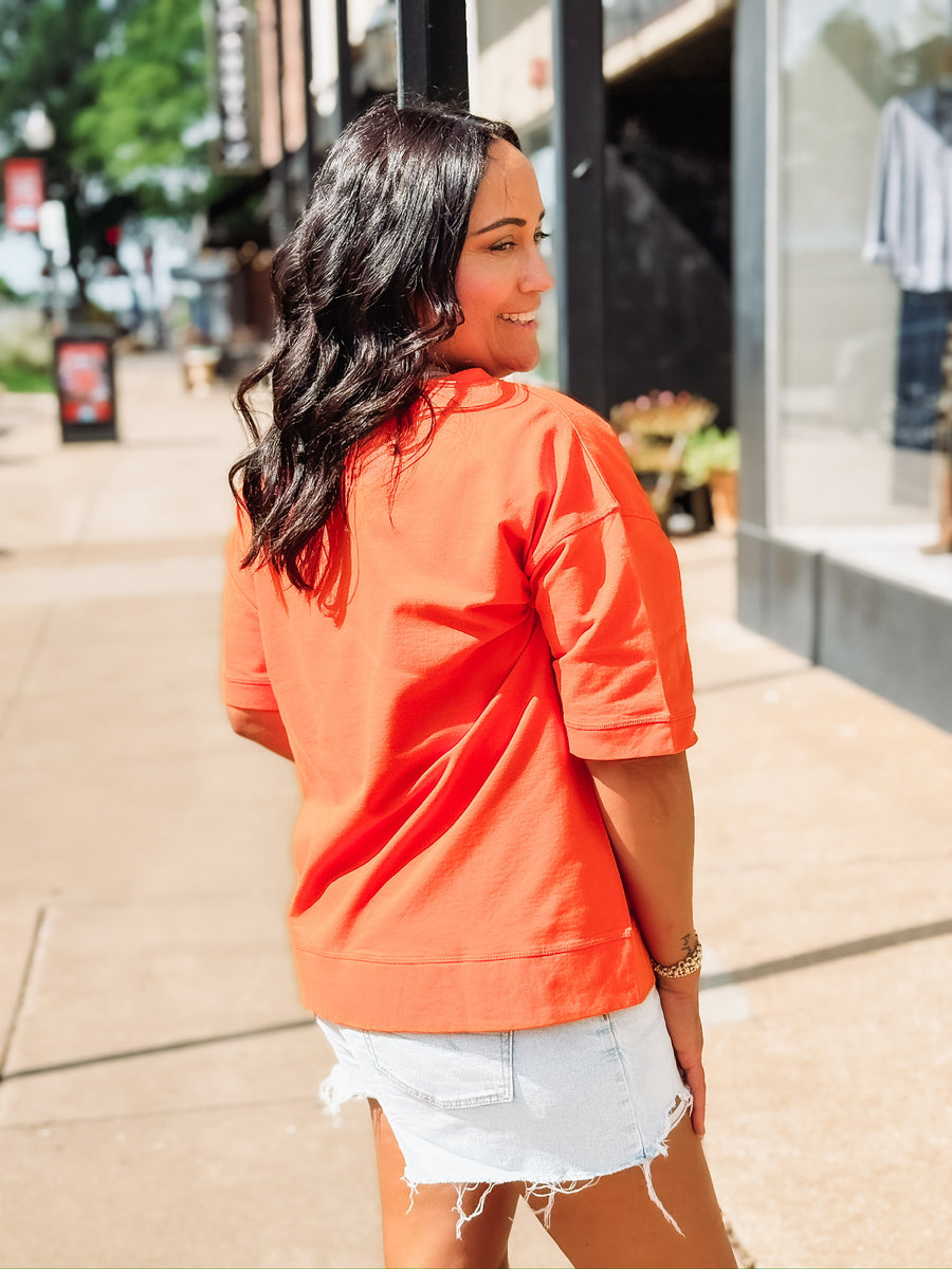 “Pistols Firing” printed in black script on an orange boxy top across the front, styled in an OSU game day theme.