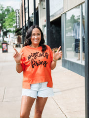 “Pistols Firing” printed in black script on an orange boxy top across the front, styled in an OSU game day theme.