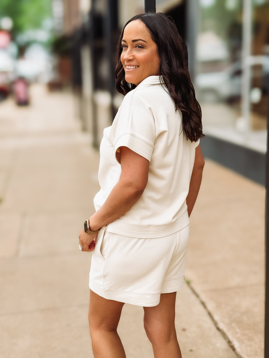 Woman in a cream colored outfit standing on a sidewalk with a blurred background