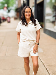 Woman in a cream outfit standing on a sidewalk with a blurred background