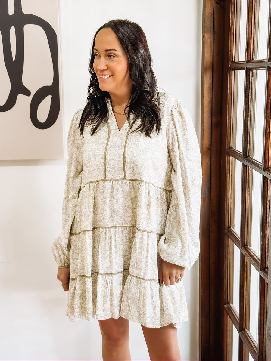 Dainty olive floral print on a cream long sleeve mini dress that features tiers and a slight v neck.