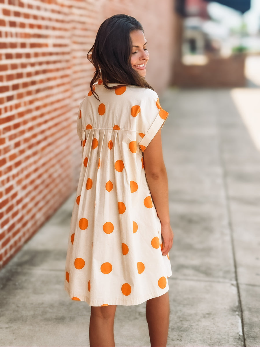 Cream mini dress with an orange polka dot print, button front closure, short sleeves, side pockets, and a relaxed fit.