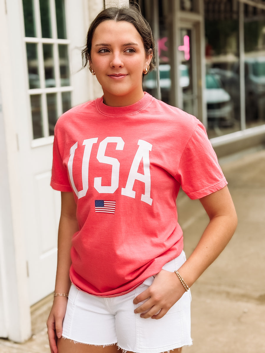 Person wearing a red 'USA' t-shirt with an American flag graphic outdoors.