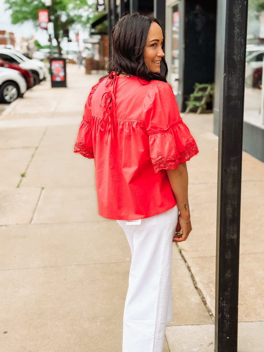 Woman wearing a red blouse and white pants on a city street.