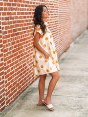 Cream mini dress with an orange polka dot print, button front closure, short sleeves, side pockets, and a relaxed fit.