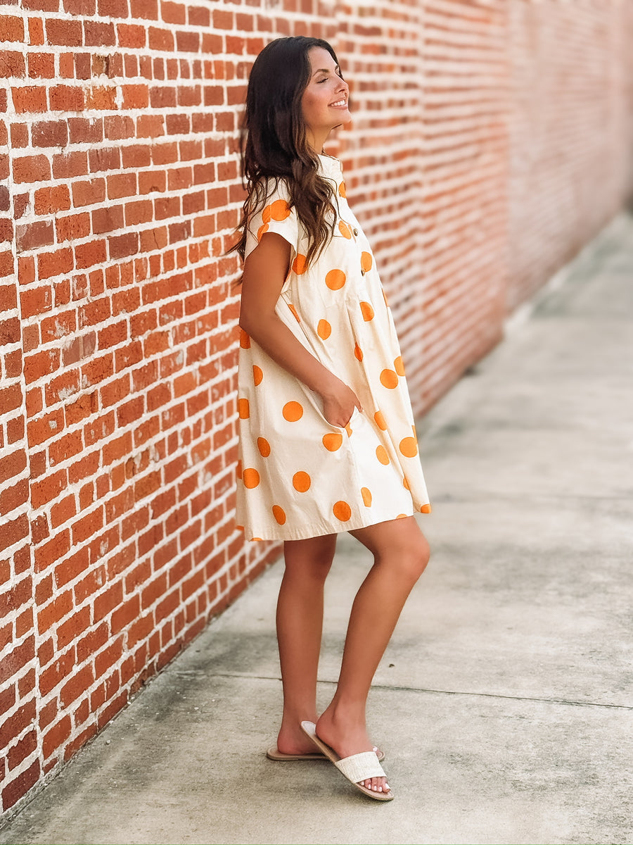 Cream mini dress with an orange polka dot print, button front closure, short sleeves, side pockets, and a relaxed fit.