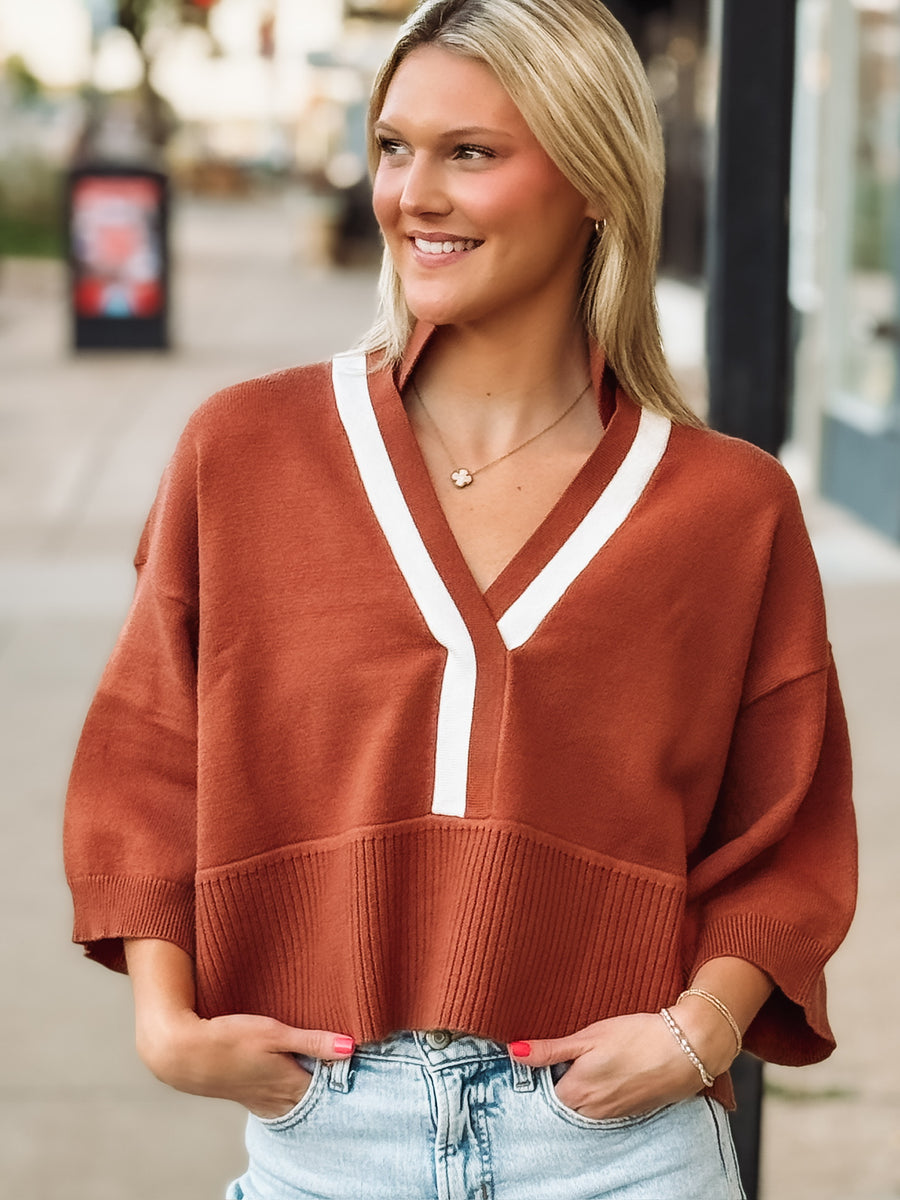 Rust drop sleeve cropped sweater with white contrast detail throughout the v neckline and front seam.