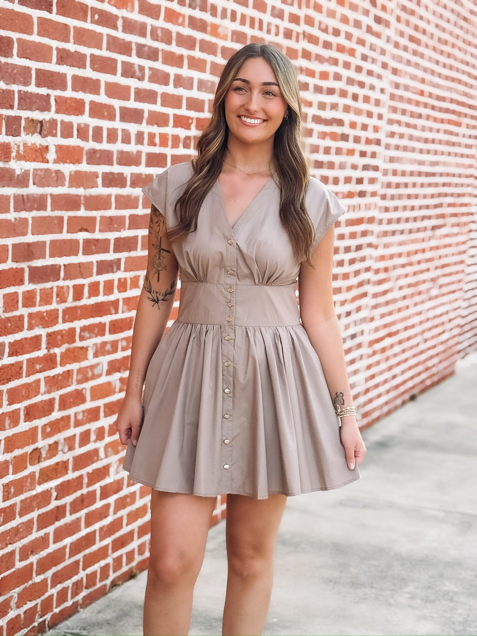 Taupe brown colored short sleeve mini dress. Features a full button front, a cinched waist and a V neckline. 