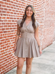 Taupe brown colored short sleeve mini dress. Features a full button front, a cinched waist and a V neckline. 