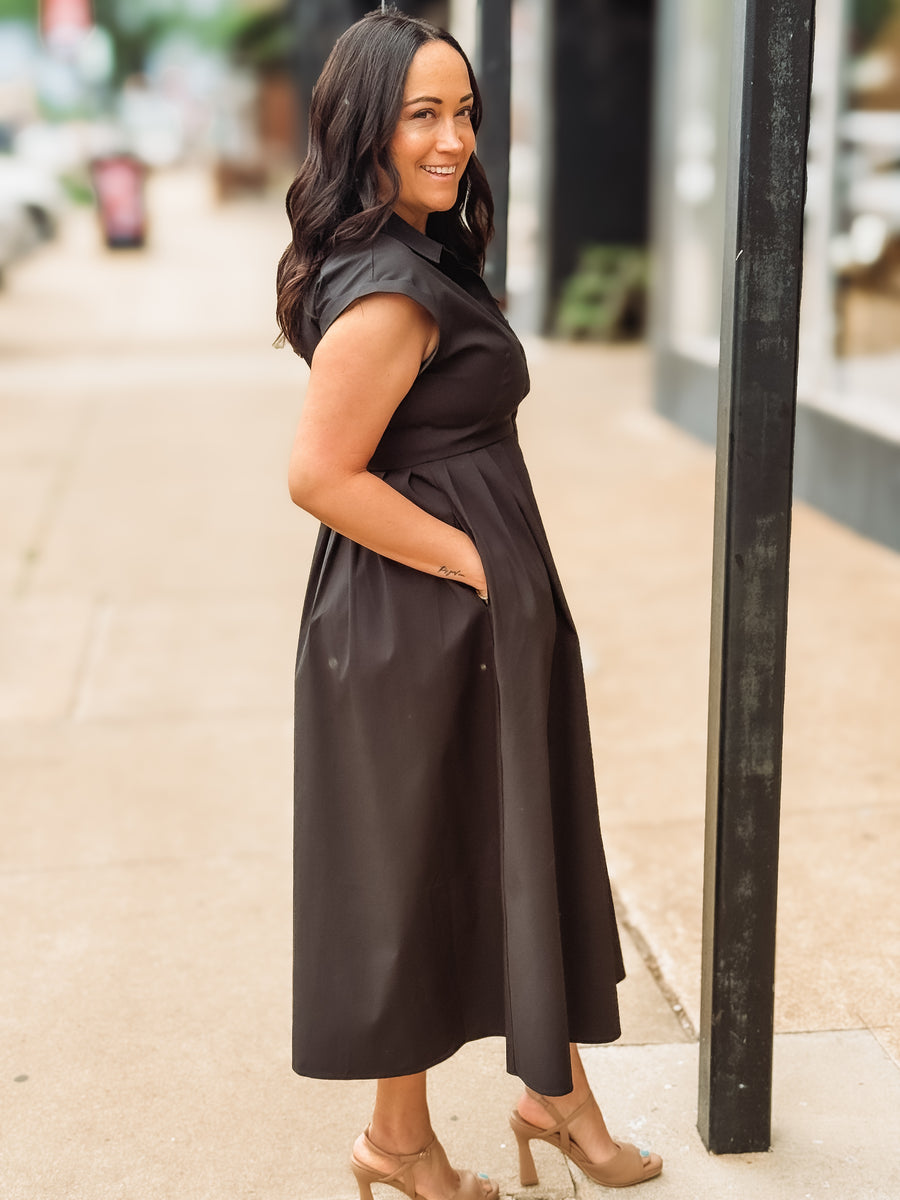 Woman wearing a black dress standing on a street corner.
