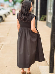 Woman wearing a black dress standing on a sidewalk.