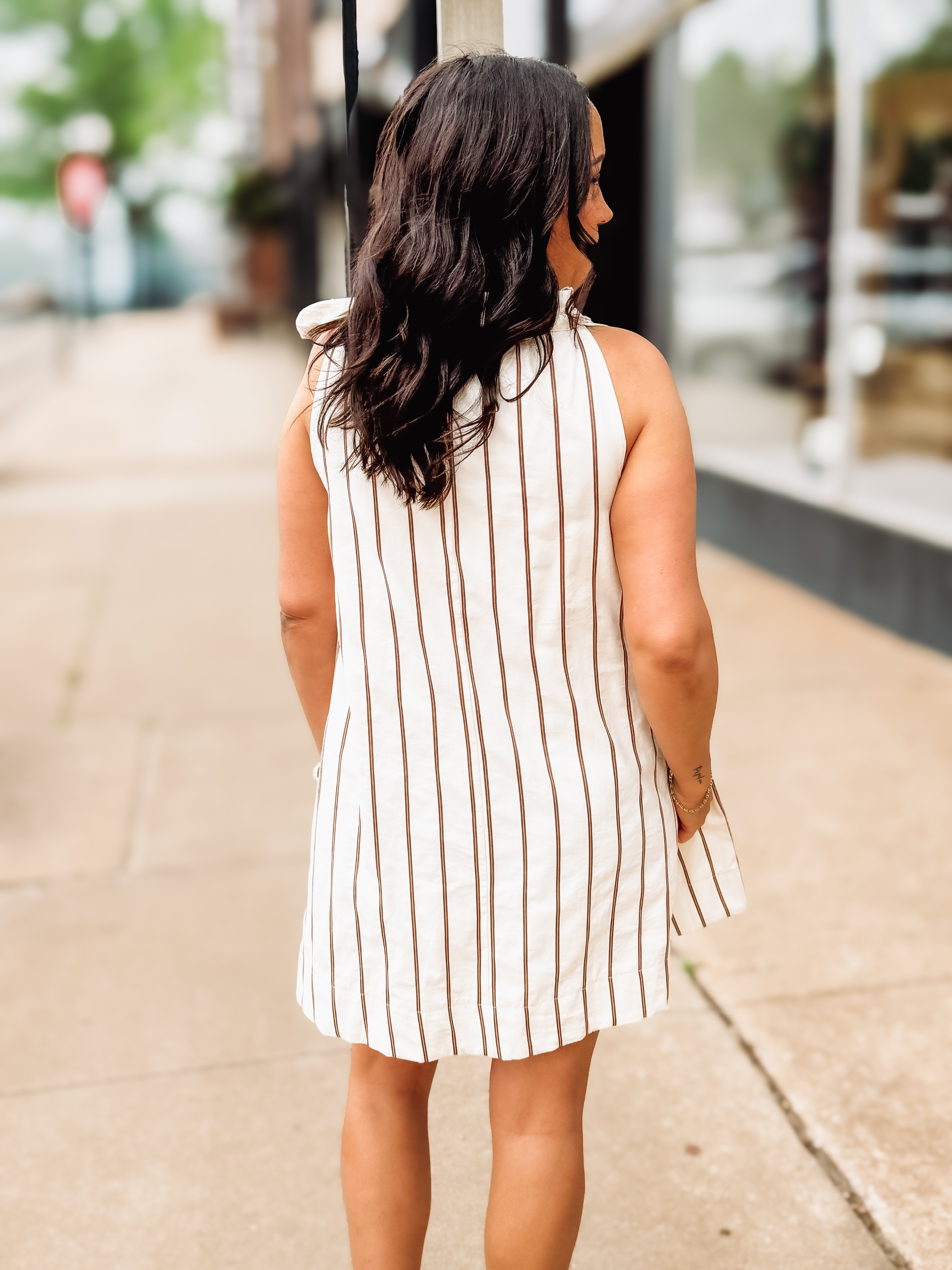 Woman wearing a white and brown striped dress on a city street.