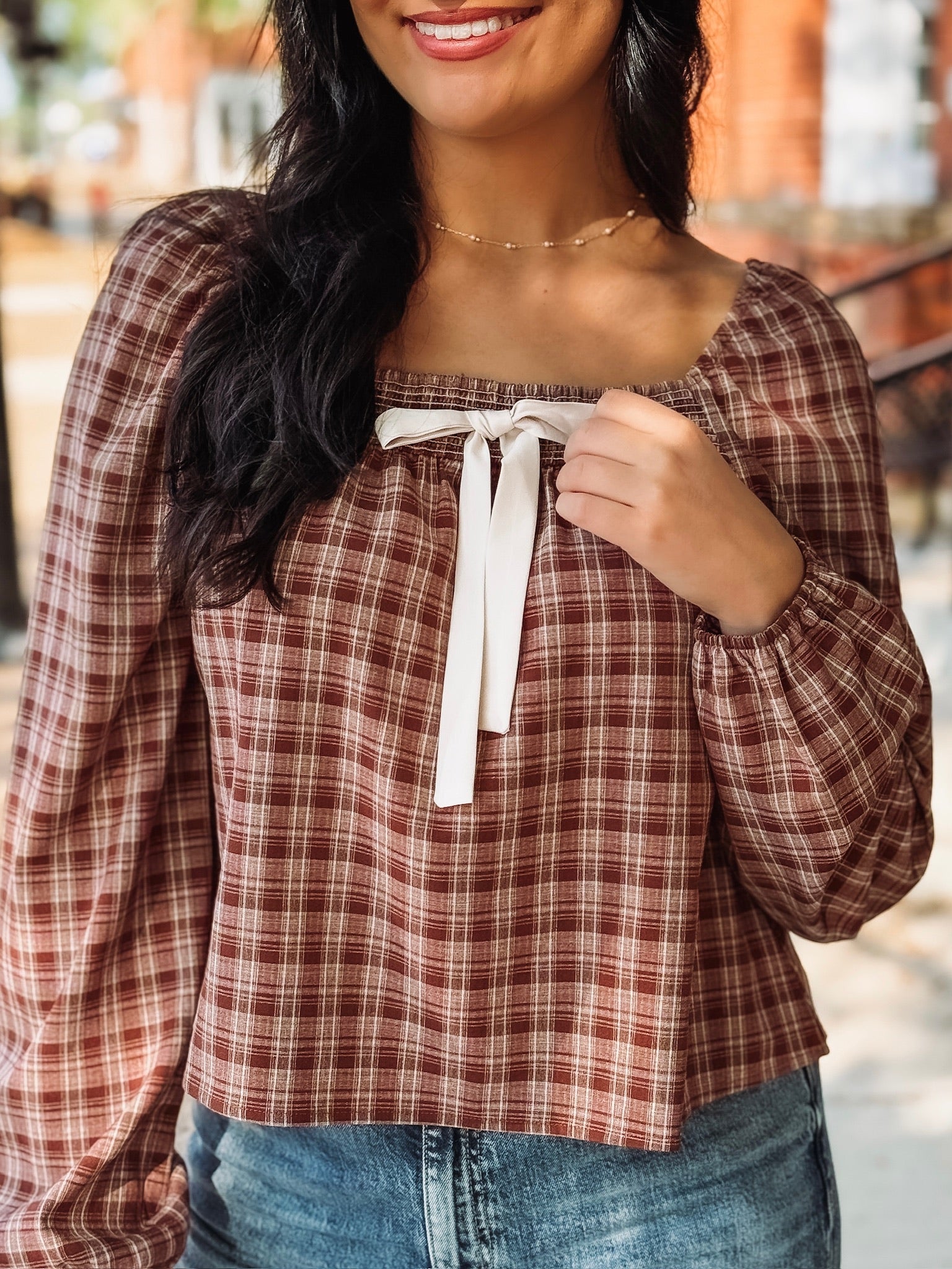 Brick and cream plaid long bubble sleeve top with a square smocked neckline and a self tie bow detail.