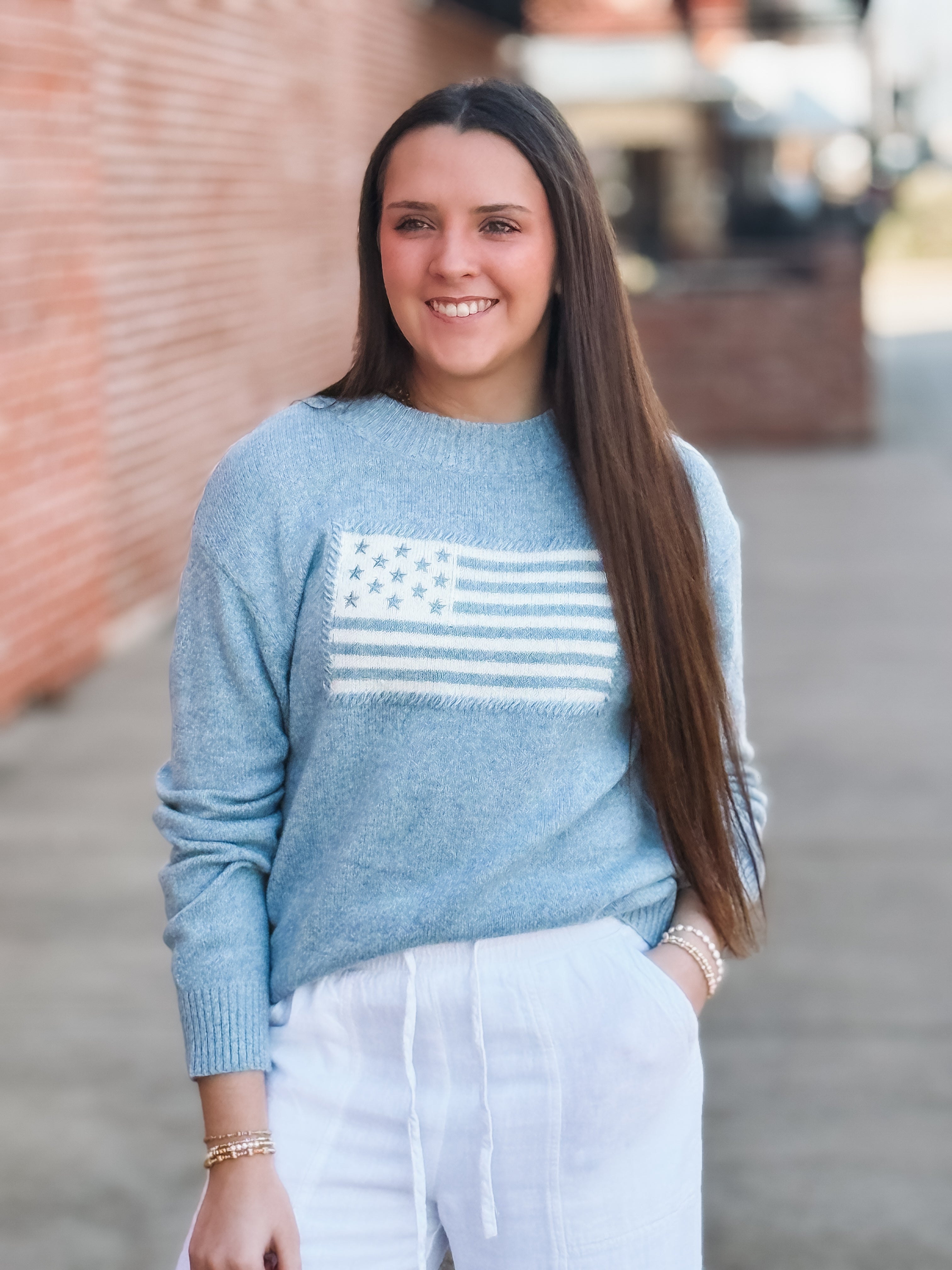 Woman wearing a blue sweater with an American flag design, standing outdoors.