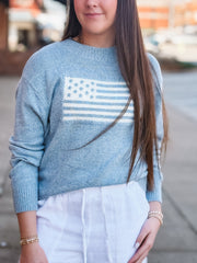 Person wearing a blue sweater with an American flag design outdoors.