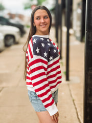 Woman wearing an American flag sweater on a city street.