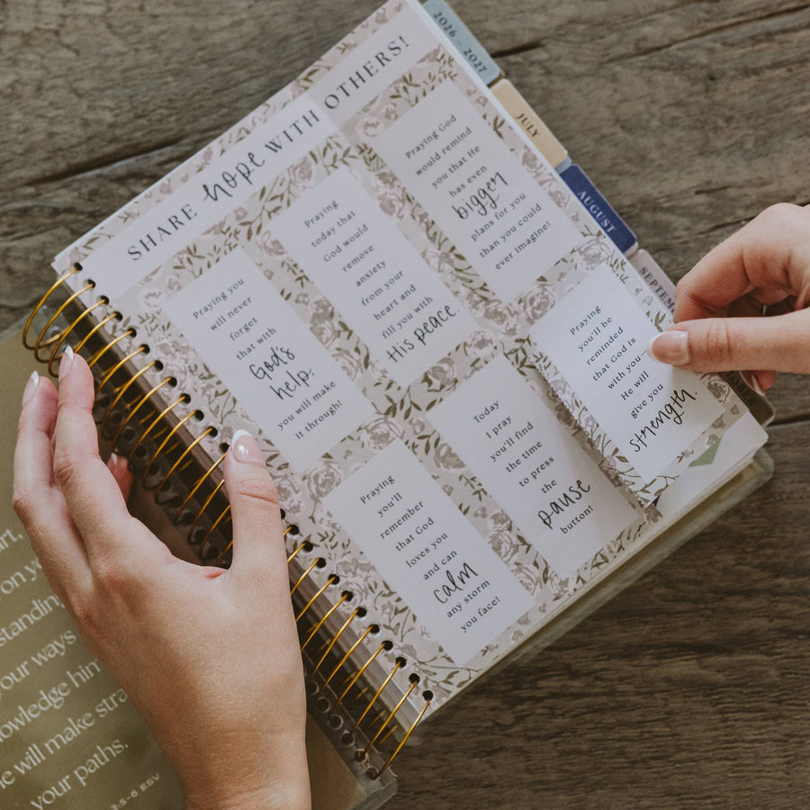 Person holding a spiral-bound notebook with printed text on a wooden surface