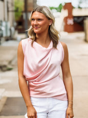 Woman wearing a pink sleeveless top and white pants outdoors.