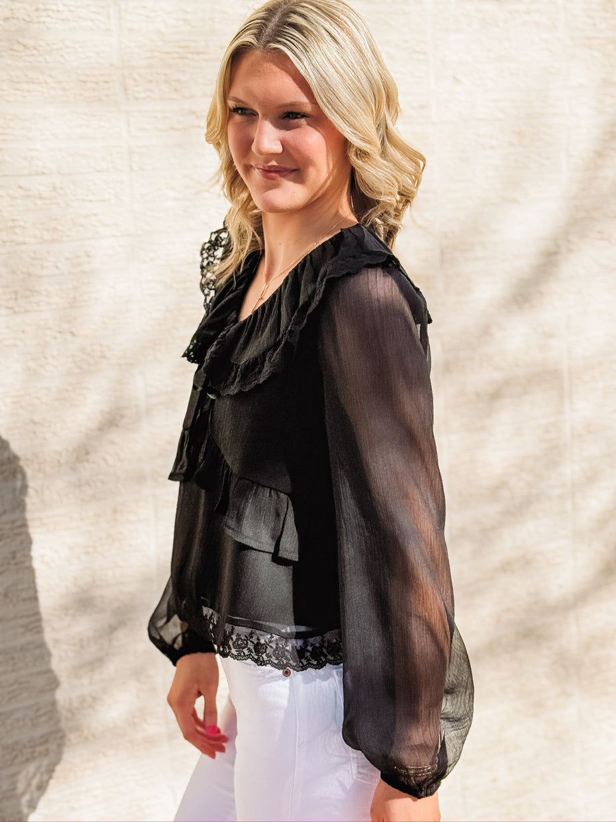 Black long-sleeve blouse featuring a wide ruffled collar with lace trim, sheer balloon sleeves, a ruffled bodice detail, and an intricate lace hemline