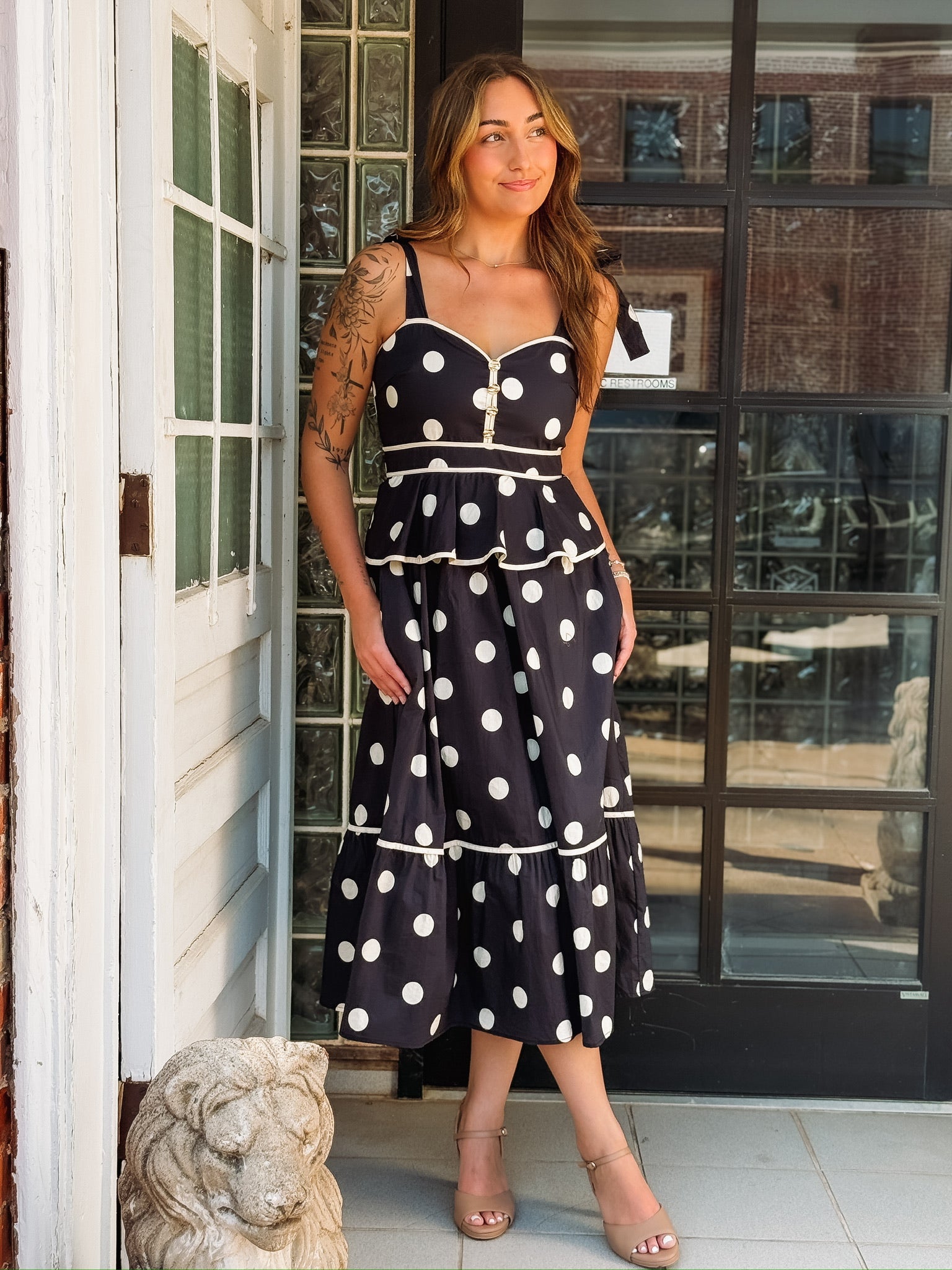 Black and white polka dot maxi dress with spaghetti straps, a tiered silhouette, and faux gold button details.
