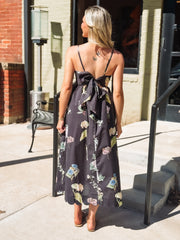 Woman wearing a floral dress standing on a sidewalk.