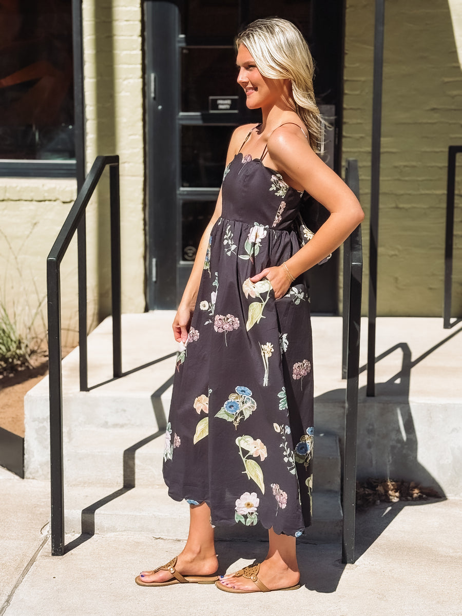 Woman wearing a floral dress standing on a sidewalk.