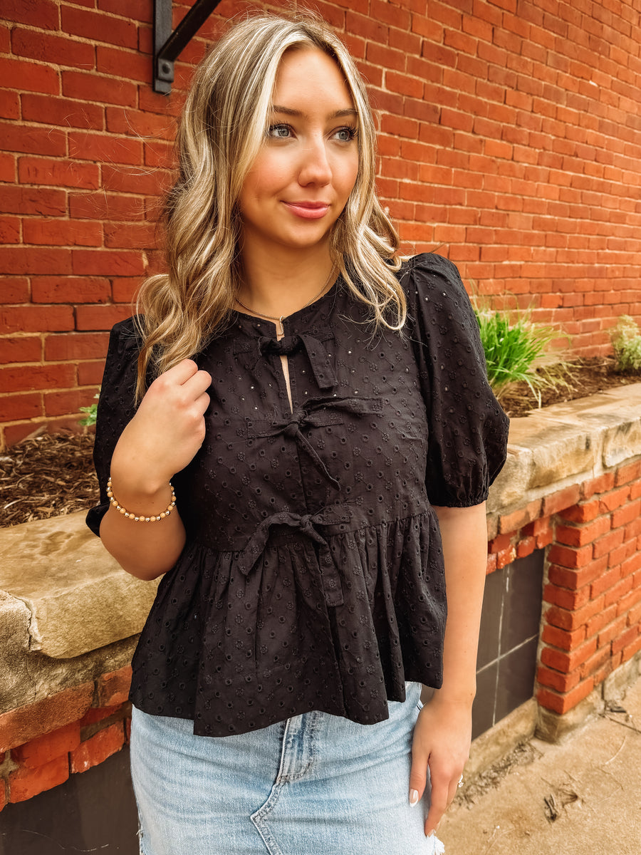 black peplum top with cut out eyelet details and bow tie front