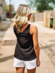 Woman wearing a black tank top and white shorts on a sidewalk.